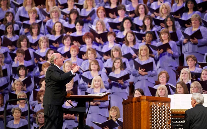 The Tabernacle Choir conductor leading the choir with women singers in purple behind him